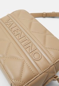 Ljust läder crossoverväska med kviltad design, präglad "VALENTINO"-logotyp och en mjuk textur. Har en avtagbar rem.