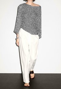 Black and white speckled knit top with an asymmetrical neckline, paired with loose white trousers and brown platform sandals.