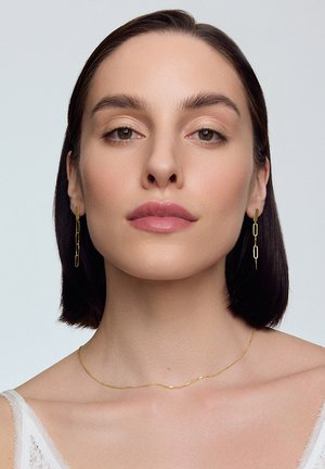 Złote kolczyki w kształcie spinaczy do papieru oraz delikatny złoty naszyjnik z łańcuszka. Gładka tekstura, minimalistyczny design i subtelny połysk na neutralnym tle.