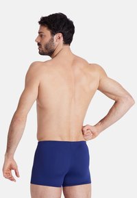 Marineblaue Schwimmshorts aus glattem Stoff; tailliertes Design mit einem Bund, niedrig geschnitten und mit minimalen Nähten.