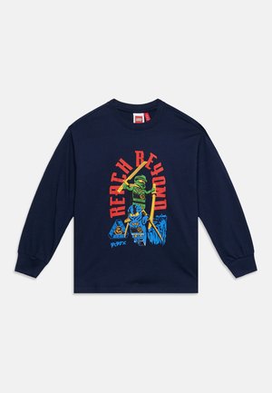 Marineblå langærmet skjorte med farverige LEGO-ninjafigurer og rød tekst ""Reach Beyond"" på fronten.