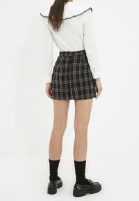 Svart och vit rutigt minikjol med en texturerad yta, med hög midja och rak fåll, i kombination med en vit blus och svarta loafers.