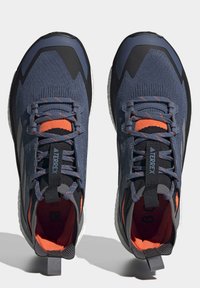 Blaue Sportschuhe mit schwarzen Akzenten, strukturiertem Mesh-Obermaterial, orangefarbenem Innenfutter und grauen Schnürsenkeln. Verfügt über eine verstärkte Ferse und Branding.