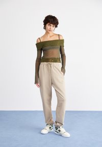 Grünes, schulterfreies Mesh-Top mit gerippten Akzenten, kombiniert mit beigen Jogginghosen mit elastischem Bund und weißen Sneakers mit grünen Akzenten.
