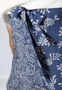 Donkerblauwe spijkerbroeken schort met witte bloemen- en paisleypatronen, voorzien van een strik in de taille en een gestructureerde stof.