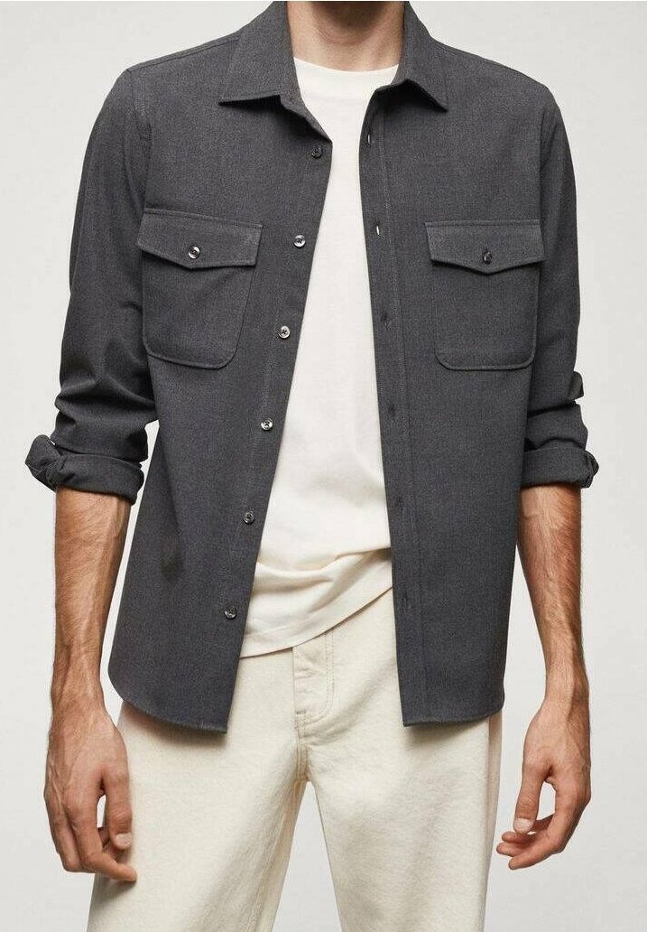 Homme portant une surchemise gris foncé à poches boutonnées, un t-shirt blanc et un jean crème. Manches retroussées, montré des épaules jusqu'au milieu des cuisses.