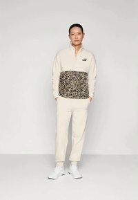 Πουλόβερ από φλις με 1/4 φερμουάρ σε κρέμα με πάνελ λεοπάρ. Συνδυασμένο με αντίστοιχες φόρμες. Λευκά αθλητικά παπούτσια. Απλός, καθημερινός σχεδιασμός.