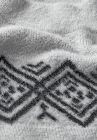 Lichtgrijze gebreide stof met een zachte textuur heeft een geometrisch zwart patroon langs de onderste rand, wat een gezellige, gelaagde uitstraling benadrukt.