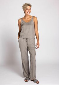 Hellgraues ärmelloses Oberteil und dazu passende locker sitzende Hose, beide aus einem weichen, glatten Stoff. Kombiniert mit dunkel gemusterten Rutsch-Sandalen.