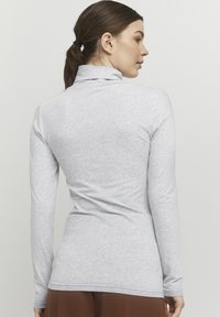 Világosszürke, hosszú ujjú galléros felső, puha, rugalmas anyagból készült. Fitted dizájn jellemzi, sima tapintással. Az alja a csípő alatt ér véget.