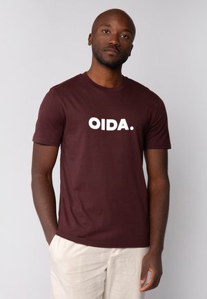 Bordeaux katoen t-shirt met korte mouwen en een ronde halslijn. Kenmerkt zich door grote witte tekst "OIDA." over de borst. Eenvoudig ontwerp met minimale details.