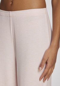 Lichtroze gestructureerde wijde broek met een elastische tailleband, die de zachte textuur en subtiele verticale lijnen op de stof benadrukt.