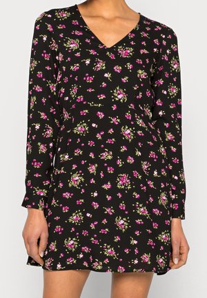Vestido negro de manga larga con estampado floral en rosa y verde, escote en V, llevado por una persona con las manos relajadas a los lados.