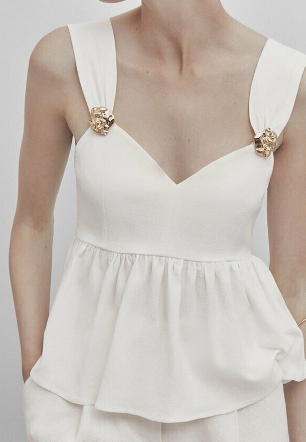 Biały top typu peplum z dekoltem w serek, szerokimi ramiączkami i złotymi akcentami na ramionach, wykonany z teksturowanej tkaniny o miękkim układzie.