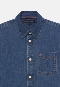 Jeansowa koszula zapinana na guziki z kołnierzykiem i kieszenią na piersi, z małą naszywką z logo Tommy Hilfiger.