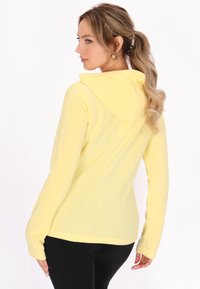 Giacca con cappuccio gialla, dal tessuto morbido, maniche lunghe e vestibilità comoda. Presenta un delicato dettaglio delle cuciture e un design informale.