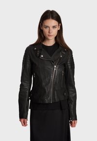 Veste de moto en cuir noir avec des accents matelassés sur les épaules, fermeture éclair asymétrique et revers à pression. Texture lisse avec deux poches zippées à l'avant.