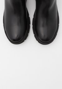 Botas de tobillo de cuero negro con un acabado suave, puntas redondeadas y suelas de goma texturizadas, con costuras laterales para un detalle adicional.