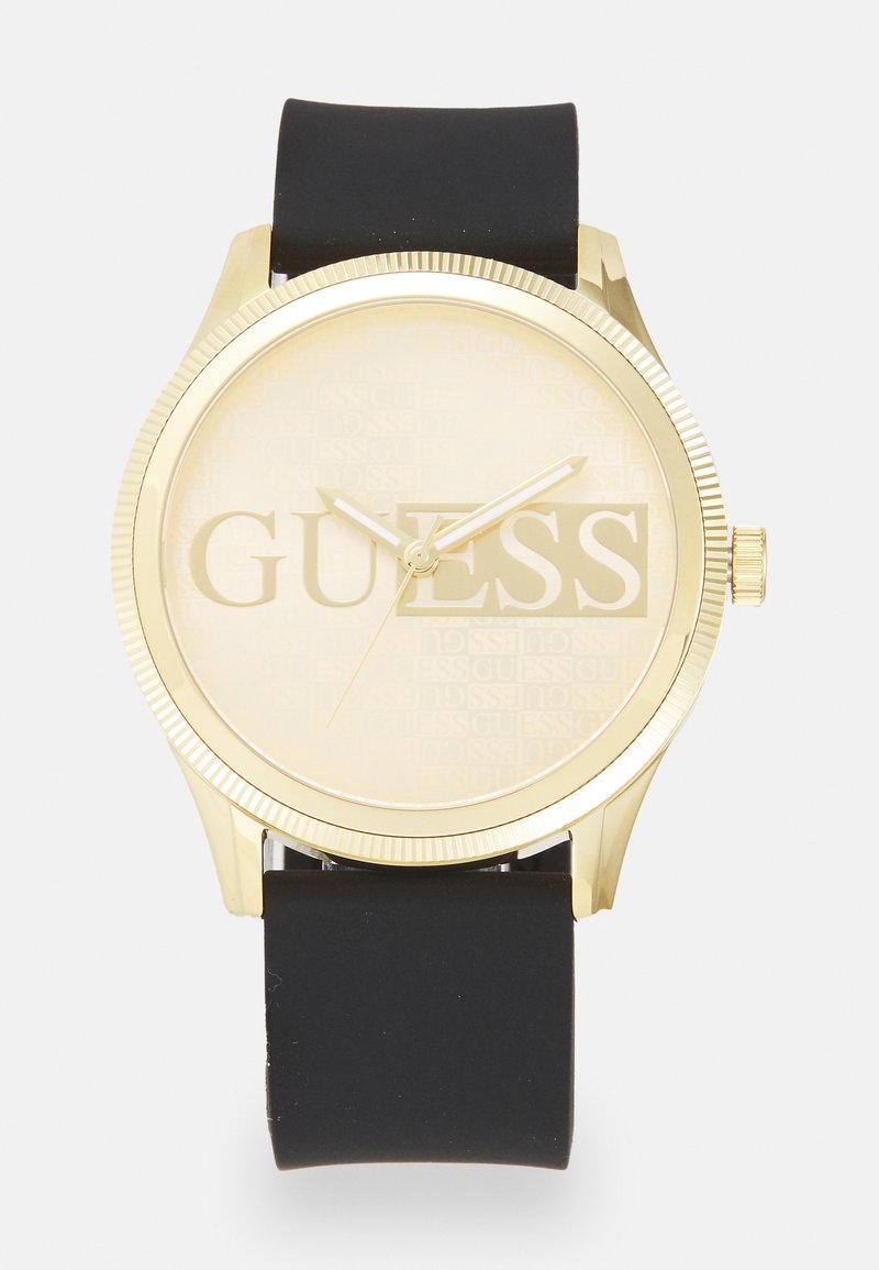 Gold-tone watch with a textured beige face, black silicone strap, and bold “GUESS” logo. Features include minimalist hands and a crown.