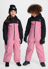 Roze en zwarte waterdichte sneeuwpakken met ritssluitingen, elastische manchetten en handschoenen, geschikt voor winteractiviteiten, gecombineerd met donkere schoenen.