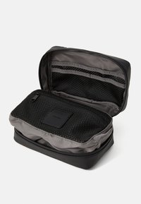 Black toiletry bag with a coated exterior, mesh pockets inside, and a zip closure. Features a gray lining and organizational compartments.