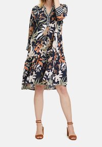 Květnaté šaty po kolena v námořnické modři s oranžovým a bílým potiskem. Mají stupňovaný design, tříčtvrteční rukávy a vzorovaný límec.