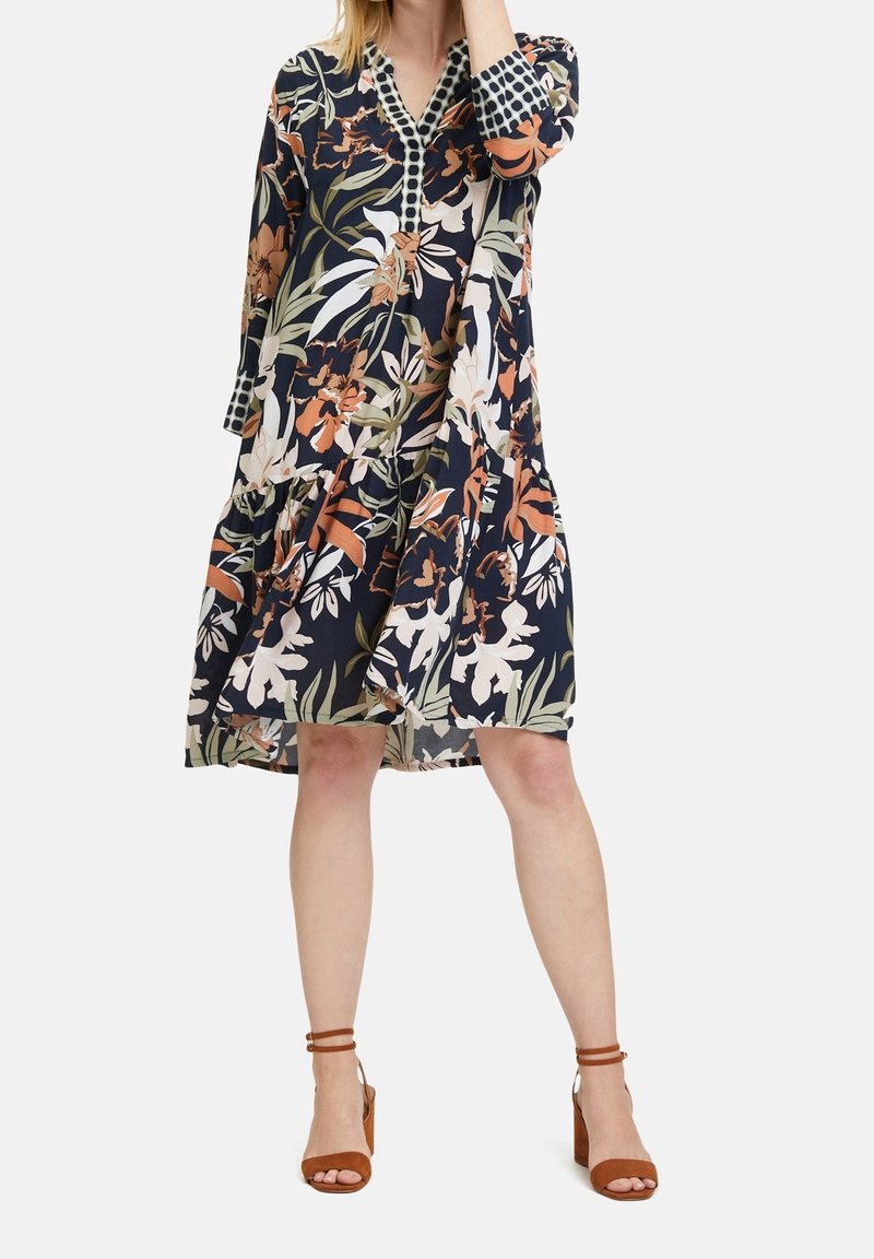 Květnaté šaty po kolena v námořnické modři s oranžovým a bílým potiskem. Mají stupňovaný design, tříčtvrteční rukávy a vzorovaný límec.