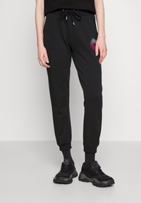 Czarne dresowe spodnie z elastycznymi mankietami, sznurkiem w talii oraz wielokolorowym okrągłym haftem na prawym udzie. Noszone z czarnymi sneakersami.