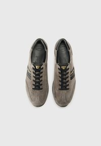 Graue Wildleder-Sneaker haben schwarze Schnürsenkel, einen schwarzen Streifen mit goldenen Akzenten und eine strukturierte Sohle. Innen sind sie mit "Super Soft" für zusätzlichen Komfort gekennzeichnet.
