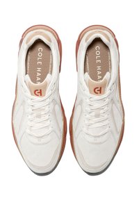 Zapatillas blancas con malla texturizada y cuero suave. Presenta una suela de goma marrón, cordones y una marca impresa en la plantilla.