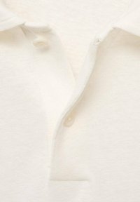 Polo shirt in cotone bianco con finitura testurizzata, dotato di una patta con tre bottoni e colletto piegato. I bottoni sono rotondi e lisci.