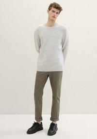 Gai pelēks adīts džemperis, brīvs piegriezums; olīvu zaļi bikses ar sarullētām piedurknēm; melni sneakers ar plakaniem zolem. Minimalistisks dizains, mīksta tekstūra.