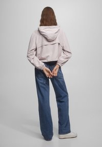 Light pink hooded jacket with elastic cuffs, layered design, and relaxed fit, paired with blue wide-leg jeans and white sneakers.