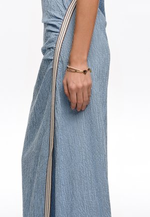 Mano de mujer con pulseras superpuestas descansando a un lado, luciendo una falda azul acanalada con una cintura a rayas en crema y negro.