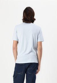 T-shirt en coton bleu clair à manches courtes, à col rond et texture lisse. Assorti à un pantalon cargo bleu foncé avec des poches angulaires.