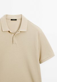 Polo beige à manches courtes avec col et patte de boutonnage à deux boutons, fabriqué en tissu texturé, posé à plat sur fond blanc.