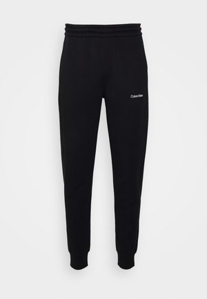 Pantalons de jogging noirs en tissu doux, avec une taille élastique et un petit logo blanc sur le côté gauche, coupe ajustée aux chevilles.