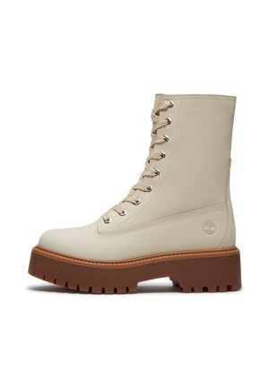 Stivale beige in pelle con lacci, suola spessa marrone a carrarmato e logo Timberland sul lato, mostrato dal lato esterno.