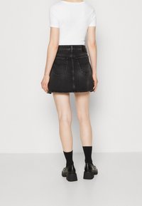 Černá džínová minisukně s mírným rozšířením, s dvěma zadními kapsami a neupraveným lemem. Kombinováno s bílým topem a černou obuví.