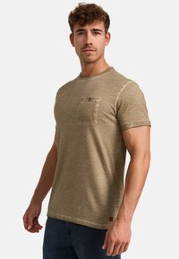Oliven grøn t-shirt lavet af blødt, struktureret stof. Har en brystlomme med en knapdetalje. Korte ærmer og rund halsudskæring.