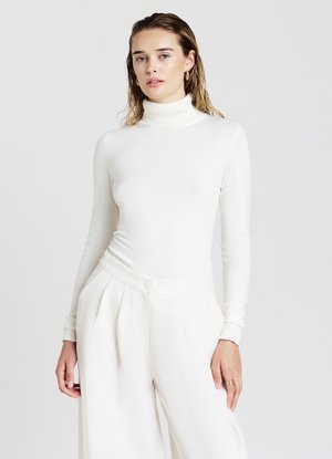 Maglione a collo alto bianco con maniche lunghe abbinato a pantaloni bianchi a gamba larga. Texture liscia, design aderente e stile minimalista.