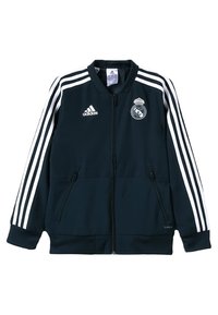 Sort Adidas zip-up sportsjakke med hvide striber på ærmerne, Real Madrid-logo på brystet og lynlåslommer foran.