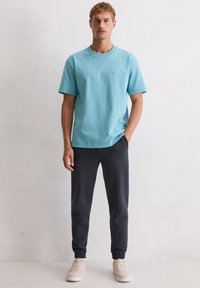 Jasnoniebieska bawełniana koszulka z krótkimi rękawami i okrągłym dekoltem, zestawiona z ciemnoszarymi joggerami z elastycznymi ściągaczami i delikatną fakturą.