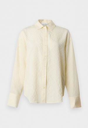 Camisa crema de manga larga con botones, con sutiles rayas verticales y puños anchos, con cuello clásico y bajo recto.