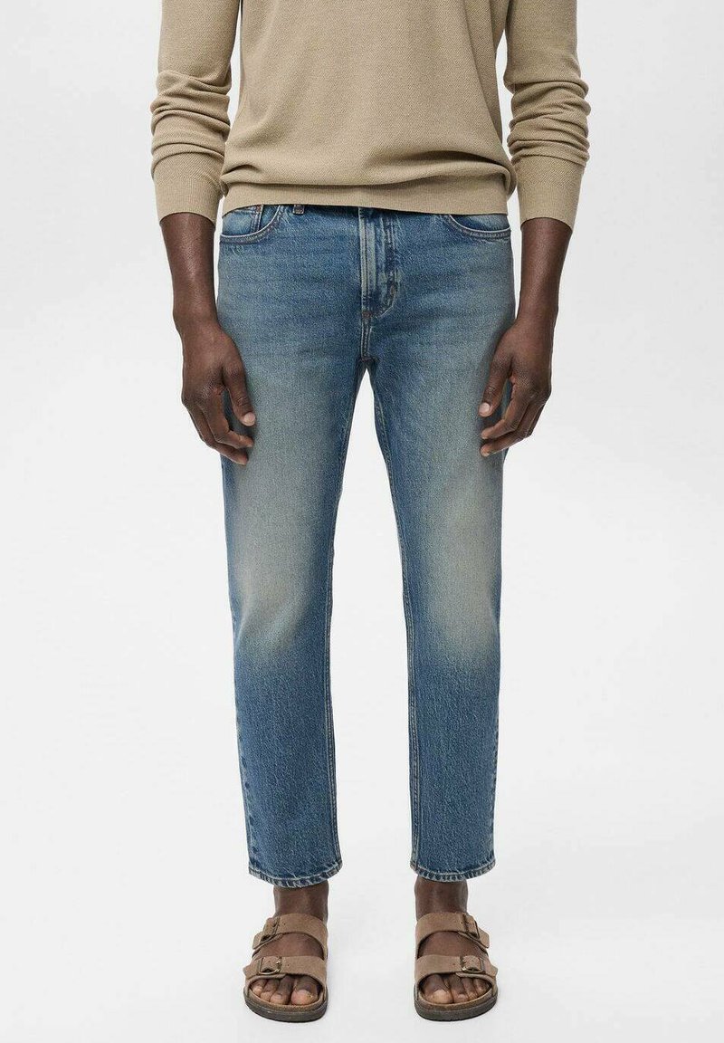 Lichtblauwe denim jeans met een tapered fit, vervaagde details en een klassiek vijf-pocket ontwerp, gecombineerd met bruine sandalen.