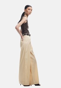 Beige wijde broek met hoge taille, voorzien van zijzakken en een zwarte riem. Gepaard met een aansluitend bruin tanktop.