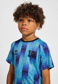 Blå och lila randig sport-t-shirt med korta ärmar, med ett svart nummer "12" och en logotyp på övre vänstra sidan.