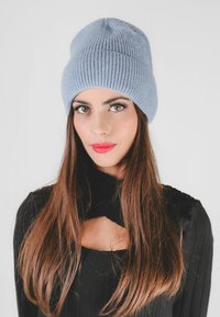 Berretto a maglia a coste di colore blu chiaro con una texture morbida, caratterizzato da una parte superiore arrotondata e una vestibilità aderente, indossato con una maglia nera a coste.