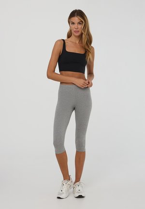 Czarny top crop z szerokimi ramiączkami, zestawiony z szarymi legginsami sięgającymi do połowy łydki. Model nosi białe buty sportowe. Prosty design i gładka tekstura.