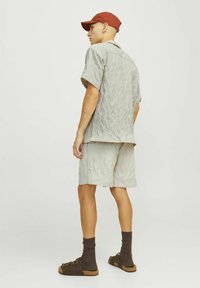 Camiseta corta de manga con textura en gris claro y pantalones cortos a juego de corte relajado, combinados con sandalias marrones y calcetines oscuros. Gorra roja.